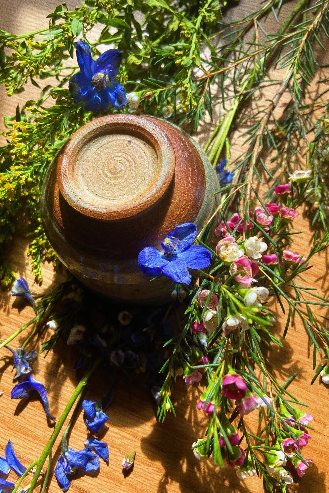 Wood-fired handmade cacao bowl with natural ceramic texture with the base facing up surrounded by flowers